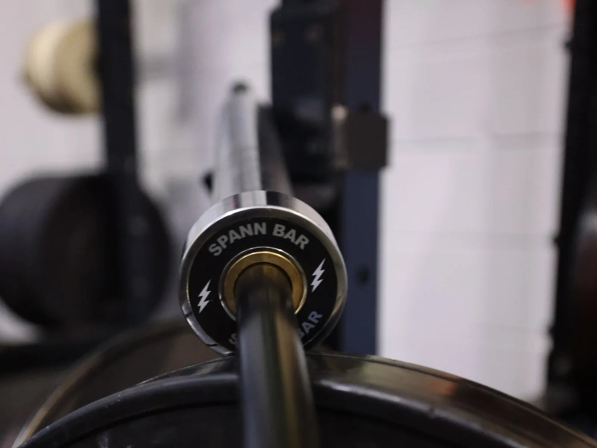 Spann Bar: The Spann Bar end cap, silver lightning bolts, above a Rogue bumper plate in the rack.