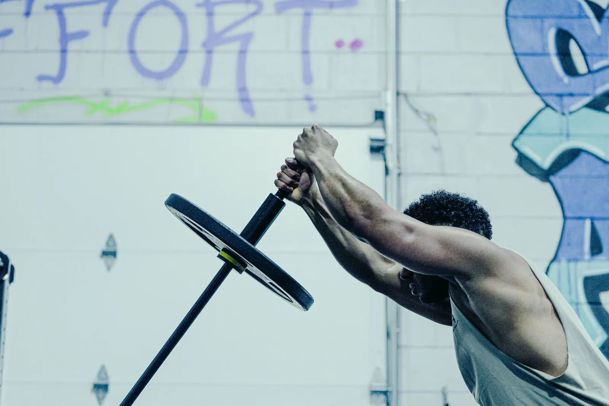 Melo Bar: An athlete pressing the loaded Melo Bar overhead with both hands under the EFFORT wall.
