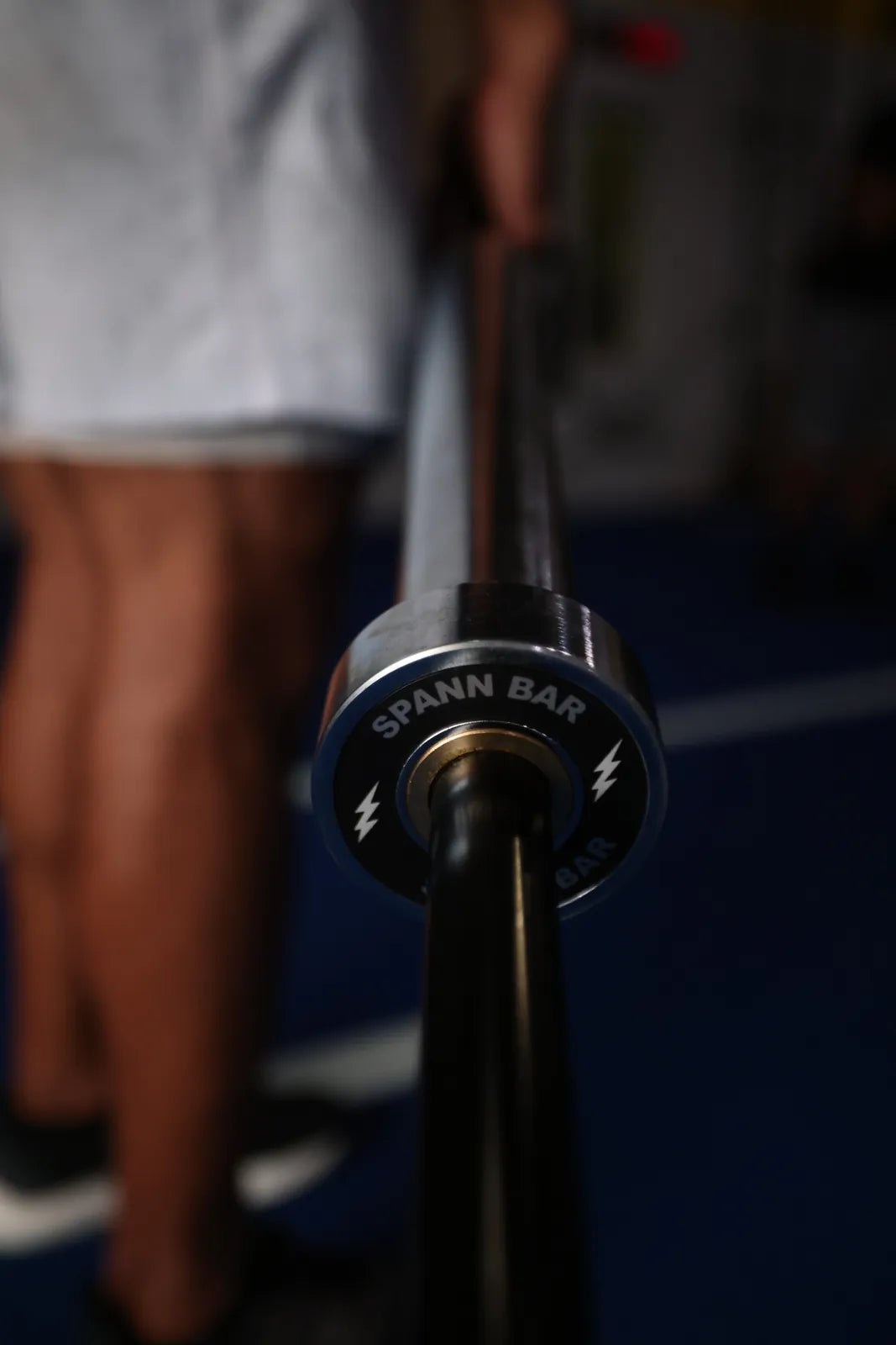 Spann Bar: A hand on the loadable end of the Spann Bar, the silver-bolt cap toward the camera, on blue turf.